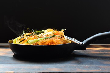 fried noodles with vegetable in a pan with black background and a chopstick.