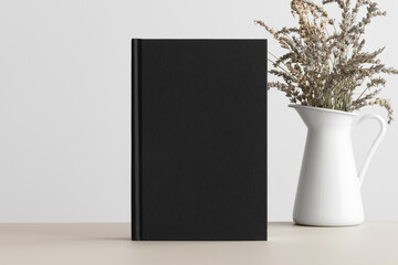 Black book mockup with a lavender decoration on the beige table.