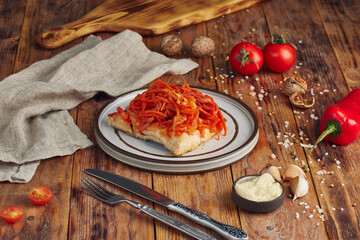 A portion of battered pan-fried hake fish fillet, wooden background with a napkin