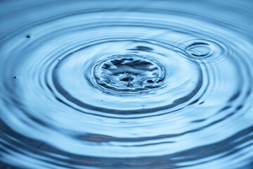 Close up view of Drops making circles on blue water surface isolated on background.