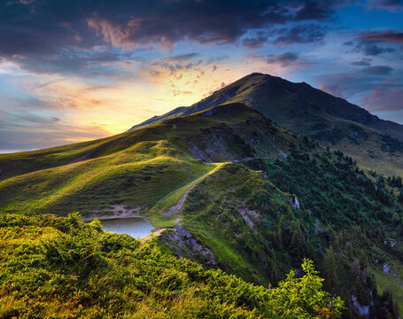 Amazing landscape of glacier Vinderel Lake and Farcau Peak at the sunset. Grassy slopes and forested hills illuminated with evening sunshine. Carpathian. Maramures. Romania. Europe.