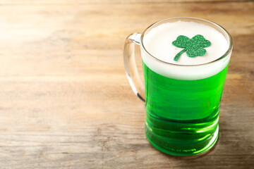 Glass of green beer with clover leaf on wooden table, space for text. St Patrick's Day celebration