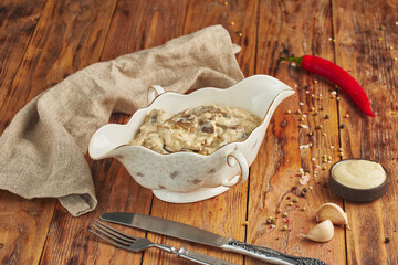 Julienne with chicken, mushrooms and cheese in a ceramic bowl, wooden background