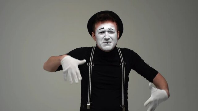 Middle shot portrait of suffering male mime slowly raises hands to face, in pain and crying. Talented actor wearing hat and gloves showing pantomime on white background. Shooting in slow motion.