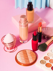 Different make up beauty cosmetics products on pink pastel background. Foundation, lipstick, eye shadows, brushes, face powder, eyeliner - 416605989