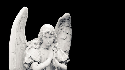 Guardian angel sculpture with open wings isolated on wide banner black background with empty text space. White angel sad expression sculpture with eyes down and hands together in front of chest.