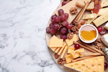 Cheese plate with honey, grapes and nuts on white marble table, top view. Space for text