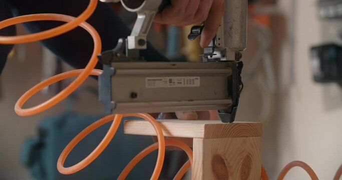 Master uses a pneumatic hammer to fasten the wooden planks, work with pneumatic tool, production of furniture and interior items, carpentry in the workshop, 4k DCI 60p Prores 422 HQ 10 bit