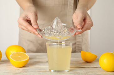 Woman pouring freshly squeezed lemon juice in glass at white wooden table, closeup