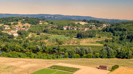 Fototapeta na wymiar Agricultural landscape in France. Panoramic view of the harvest fields with the round hay bales, green hills and a village in the background.