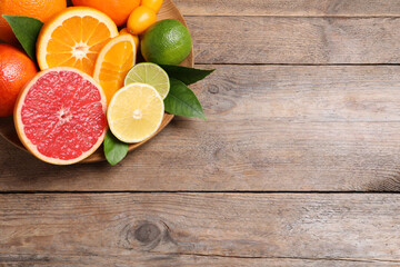Fresh juicy citrus fruits with green leaves on wooden table, top view. Space for text