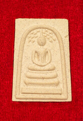 Macro Thai buddha amulet on the red velvet background.	
