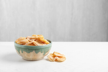 Delicious dried jackfruit slices in bowl on white wooden table. Space for text