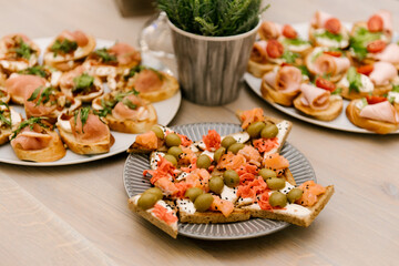 Delicious spicy tomato Italian snacks, or bruschetta, on slices of toasted baguette, decorated with basil, red fish, ham on a wooden board