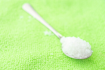 White sea salt in spoon on the green towel.