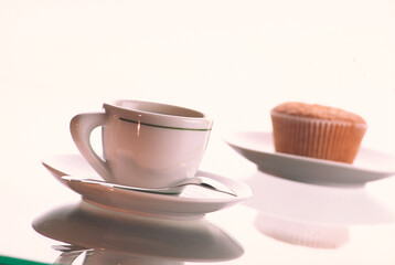 Fototapeta na wymiar Cupcake in a plate on a blurred light background and a coffee cup with a spoon in a plate.