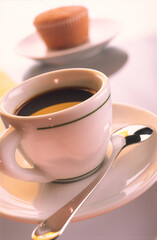 Cupcake in a plate on a blurred light background and a coffee cup with a spoon in a plate.