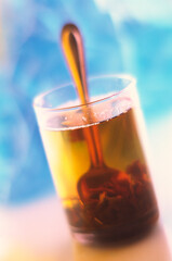 glass of hot tea with a spoon stands on the table and a blurred blue background.