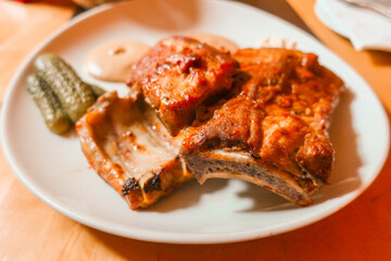 hot baked ribs with pickled cucumbers on a white plate served as a second in a restaurant