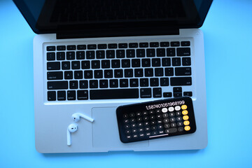 The laptop with phone-calculator and air pods on blue background 