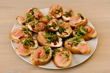 Delicious spicy tomato Italian snacks, or bruschetta, on slices of toasted baguette, decorated with basil, red fish, ham on a wooden board