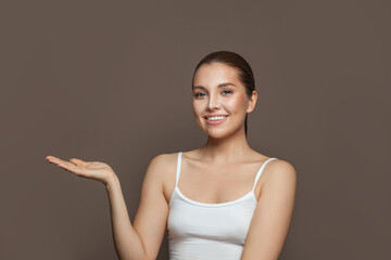 Healthy young woman with clear skin smiling and showing empty open hand on brown background