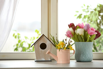 Beautiful spring flowers with birdhouse on window sill