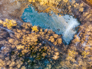 Aerial drone winter scenery on frozen wintery small wild lake in forest in warm sunset light. Fly...