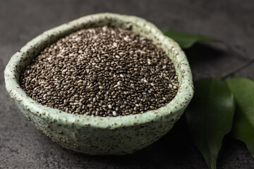 Bowl with chia seeds and leaves on grey table, closeup