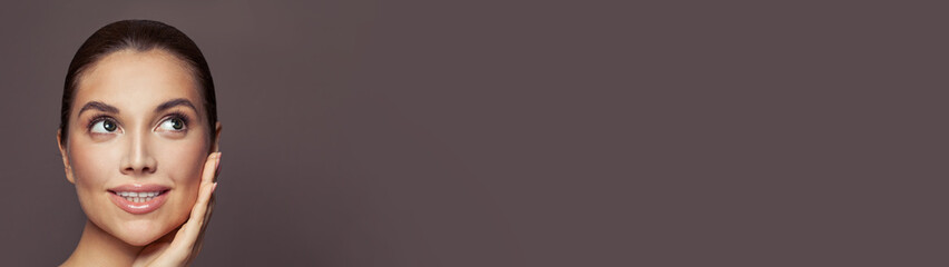 Young cute female face on brown banner background with copy space. Healthy model woman smiling and looking up