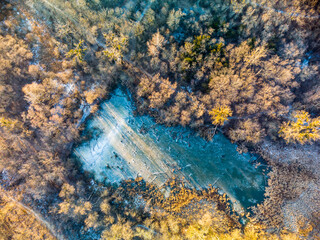 Aerial drone winter scenery on frozen wintery small wild lake in forest in warm sunset light. Fly...