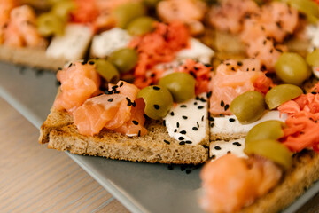 Delicious spicy tomato Italian snacks, or bruschetta, on slices of toasted baguette, decorated with basil, red fish, ham on a wooden board