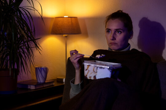 lonely sad woman eating ice cream from container while sitting on couch and watching tv at home