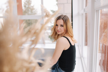 Fototapeta premium Young attractive woman in studio sit near the window. Female in denim. Home style