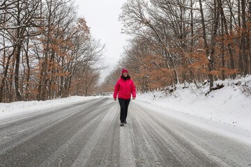 Woman walks on the white road in the snowy forest.