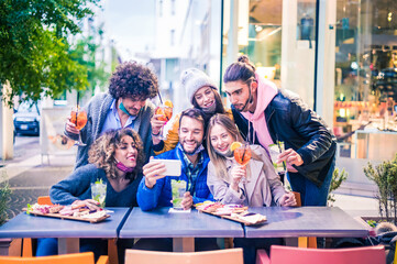 Friends taking selfie outside at cocktail bar - New normal lifestyle concept with young people having fun together at restaurant with face masks