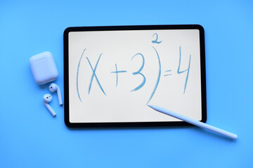 Tablet ipad with the mathematical equation inscription with apple Pencil and air pods on blue background