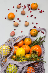 Persimmon, apples and lemon in reusable mesh bag. Lychee, cranberries and tangerines on table