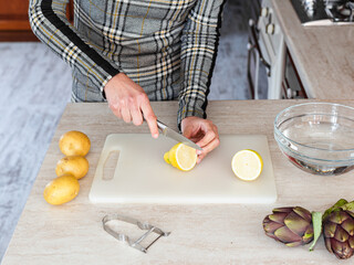 Woman cutting in half a lemon on a white plastic chopping board. Cooking at home