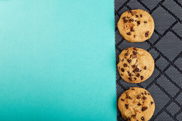 three cookies with chocolate on a black wicker napkin and blue background