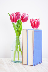 books with a flower bookmark next to a vase with tulips