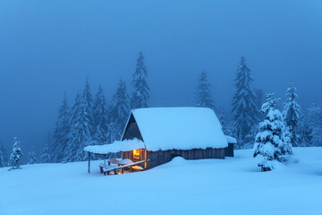 Fantastic winter landscape with glowing wooden cabin in snowy forest. Cozy house in Carpathian...