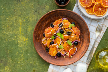 A healthy salad of sliced bloody oranges, purple onions, olives and pine nuts with olive oil dressing on a brown plate against an olive concrete background. Vegan recipes.