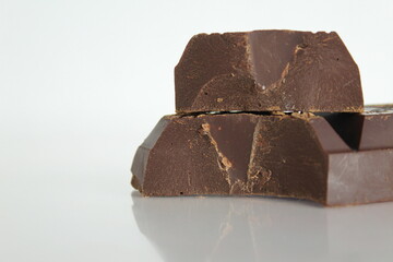 Dark bitter chocolate pieces stacked slide lies on a white background with a reflection with a place for text and copyspace