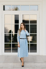 Fototapeta premium Attractive young girl on the background of the white house in a blue dress