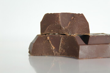 Dark bitter chocolate pieces stacked slide lies on a white background with a reflection with a place for text and copyspace
