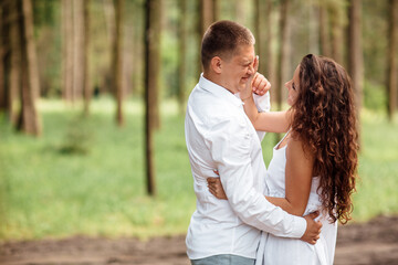 Fototapeta premium A couple in love beautiful young man and woman are hugging in a summer park on a sunny day. Date outside, well dressed, so excited and lovely