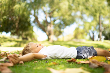 Little boy lying on the grass looking up at the trees. 