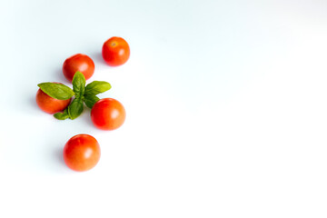 Red cherry tomatoes with green basil on a white background