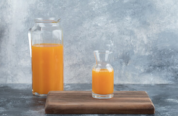 Glass and jug of orange juice on wooden board